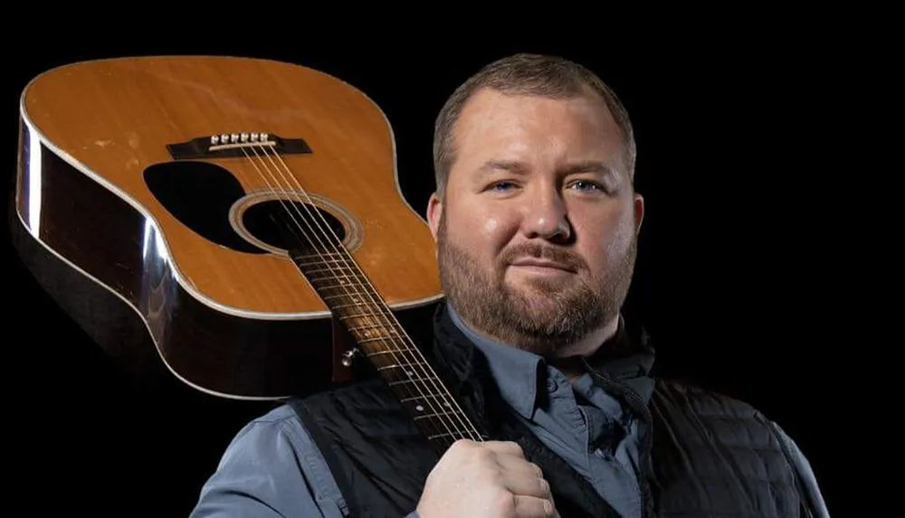 A man with a beard is posing confidently with a guitar against a black background