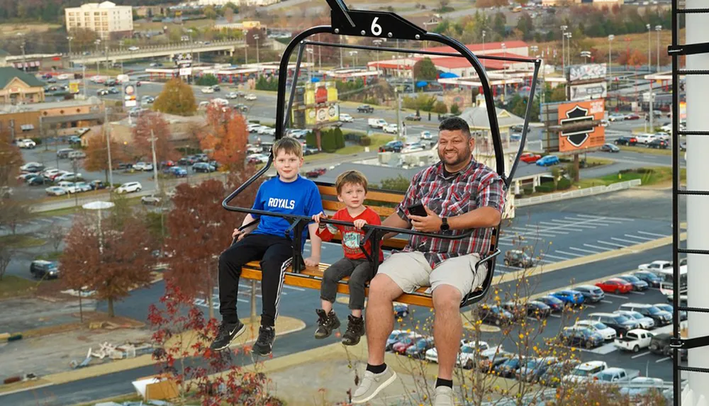A man and two children are riding on a chairlift with a cityscape in the background