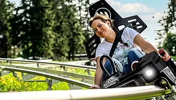 A person is enjoying a ride on an alpine coaster amidst green surroundings on a sunny day.