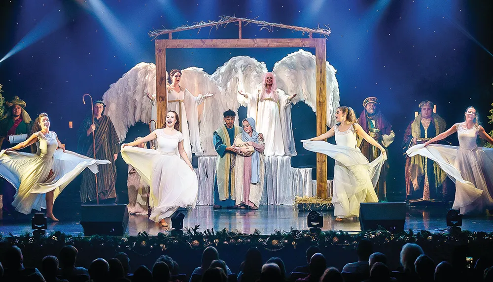 A theatrical depiction of the Nativity scene features actors dressed as angels shepherds and dancers with a central focus on Mary Joseph and baby Jesus