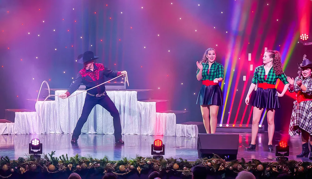 A performer in a cowboy outfit skillfully twirls a lasso on stage while a group of smiling women in festive attire watches him against a colorful lit-up background
