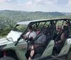 Three people are enjoying a rain-soaked ride in an off-road vehicle with the driver and one passenger smiling widely as they are splashed with water