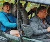 Three people are enjoying a rain-soaked ride in an off-road vehicle with the driver and one passenger smiling widely as they are splashed with water