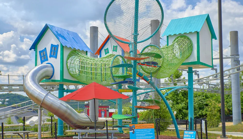 This image shows a colorful playground structure with slides and climbing nets set against a cloudy sky