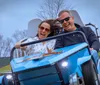 Two people are joyfully experiencing a ride in a blue roller coaster car with dynamic expressions and windswept hair