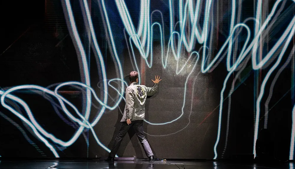 A person is interacting with a dynamic light display on a large screen in a dark room suggesting a blend of art and technology