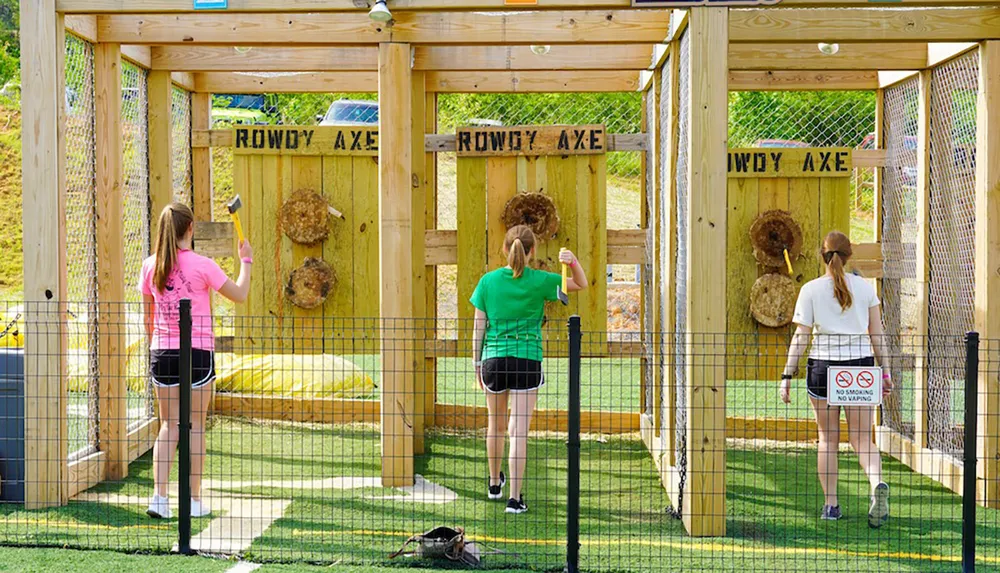 Three individuals are participating in axe throwing at an outdoor axe-throwing range
