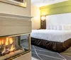 This image shows a modern hotel room with a large bed and a glass-enclosed fireplace