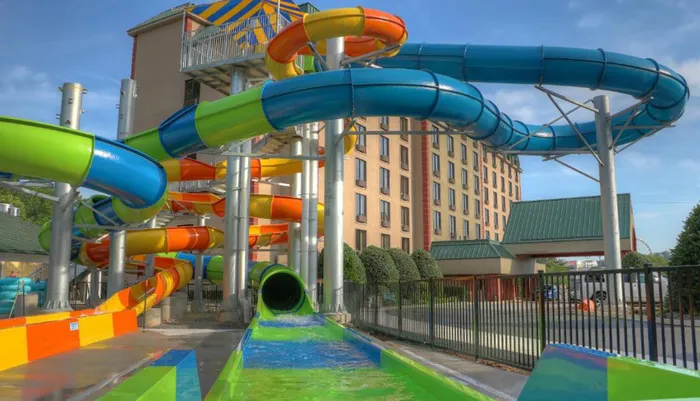 A colorful outdoor water slide complex snakes its way through the frame with a hotel in the background