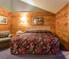 The image shows a cozy bedroom with wood-paneled walls a colorful quilt on the bed plaid upholstered furnishings and framed artwork creating a rustic ambiance