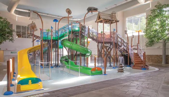 The image shows an indoor water play area with slides fountains and climbing structures designed for childrens entertainment