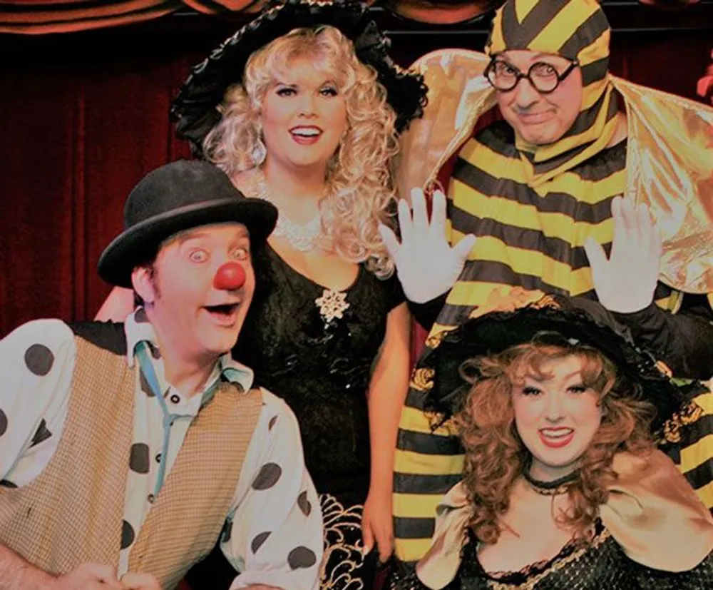 Four performers dressed in theatrical costumes smile for the camera with one dressed as a clown another as a bee and the other two in vintage-style outfits