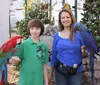 A young person and an adult are posing with a colorful red macaw and a blue hyacinth macaw perched on their arms