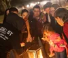 A group of people are gathered around a lantern outdoors at night paying attention to a person who appears to be leading a tour or telling a story