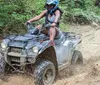 A person is riding an ATV through a muddy trail splashing water and mud as they go