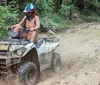 A person is riding an ATV through a muddy trail splashing water and mud as they go