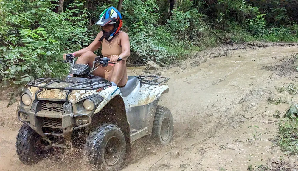 A person is riding an ATV through a muddy trail in the forest creating a splash