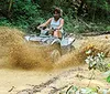 A person is riding an ATV through a muddy trail splashing water and mud as they go