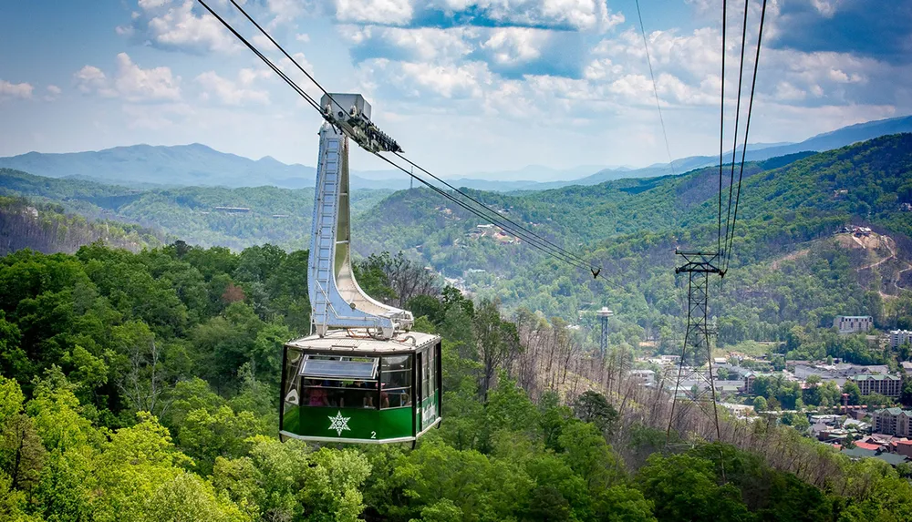 A cable car with passengers is descending a lush mountain offering scenic views of the surrounding landscape and distant hills