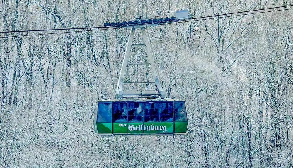 A cable car with Ober Gatlinburg written on it ascends over a snowy forested landscape