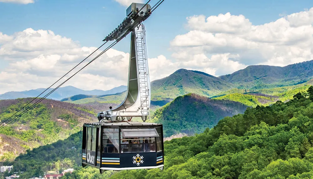 A cable car with a logo on it traverses a scenic landscape with lush green mountains and patches of residential areas below
