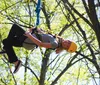 A person is joyfully zip-lining through a forest wearing a helmet and a harness for safety