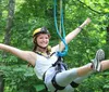 A person is joyfully zip-lining through a forest wearing a helmet and a harness for safety