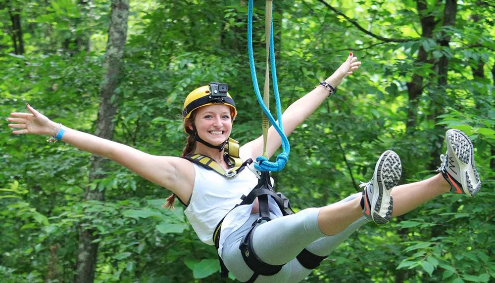 A smiling person is joyfully zip-lining through a forested area with a helmet-mounted camera recording the experience