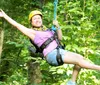 A person is joyfully zip-lining through a forest wearing a helmet and a harness for safety