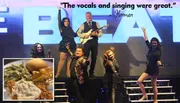 A group of performers is posing energetically on stage in front of a large sign, with a positive quote about their singing and an inset image of a meal featuring chicken, mashed potatoes, and green beans.