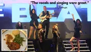 A group of performers is posing energetically on stage in front of a large sign, with a positive quote about their singing and an inset image of a meal featuring chicken, mashed potatoes, and green beans.