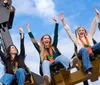 Thrilled amusement park guests are raising their hands high while enjoying the exciting motion of a ride against a blue sky