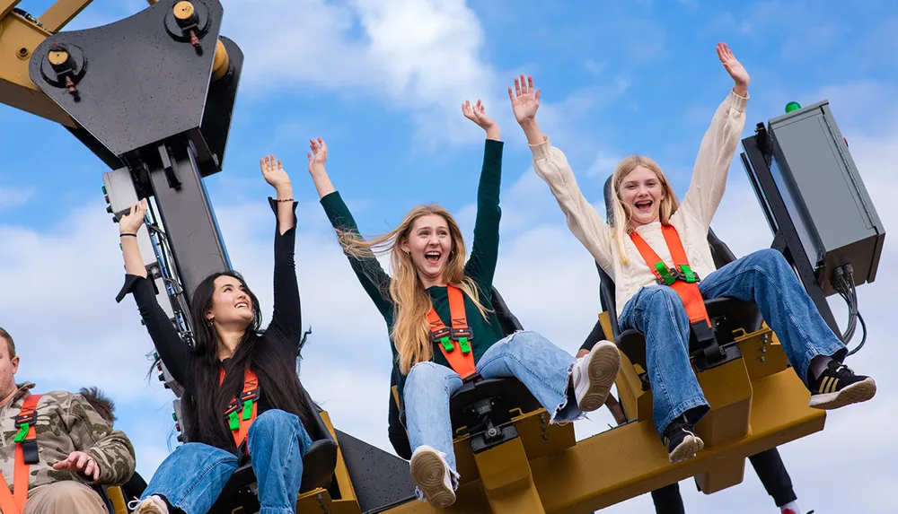 Thrilled amusement park guests are raising their hands high while enjoying the exciting motion of a ride against a blue sky