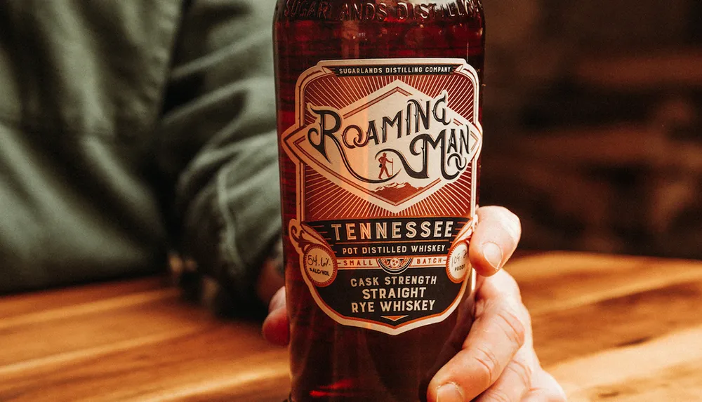 A person is holding a bottle of Roaming Man Tennessee cask strength straight rye whiskey