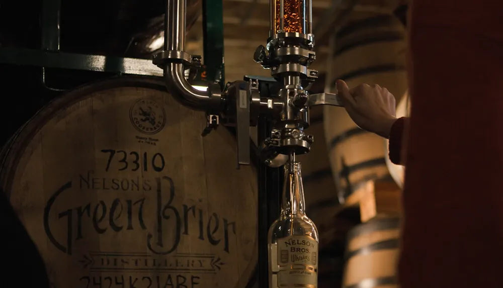 A hand is operating a valve to fill a bottle with whiskey from a barrel labeled Nelsons Green Brier Distillery