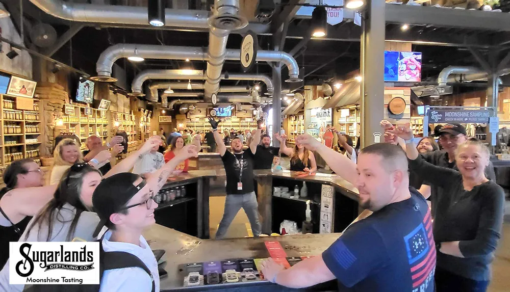 A group of people are enthusiastically raising their drinks for a toast inside Sugarlands Distilling Co during a moonshine tasting event