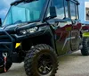 The image shows a rugged black all-terrain vehicle with large tires parked outdoors with a small inset showing an alternate view