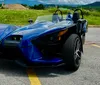 A red Polaris Slingshot three-wheeled vehicle is parked outdoors with a scenic backdrop of hills and cloudy skies