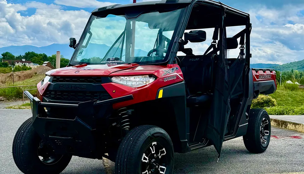 A red off-road utility vehicle is parked outdoors with mountains in the background