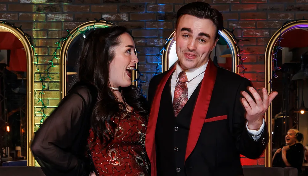A man and a woman are dressed up and engaged in a lively conversation in front of a decorated brick wall