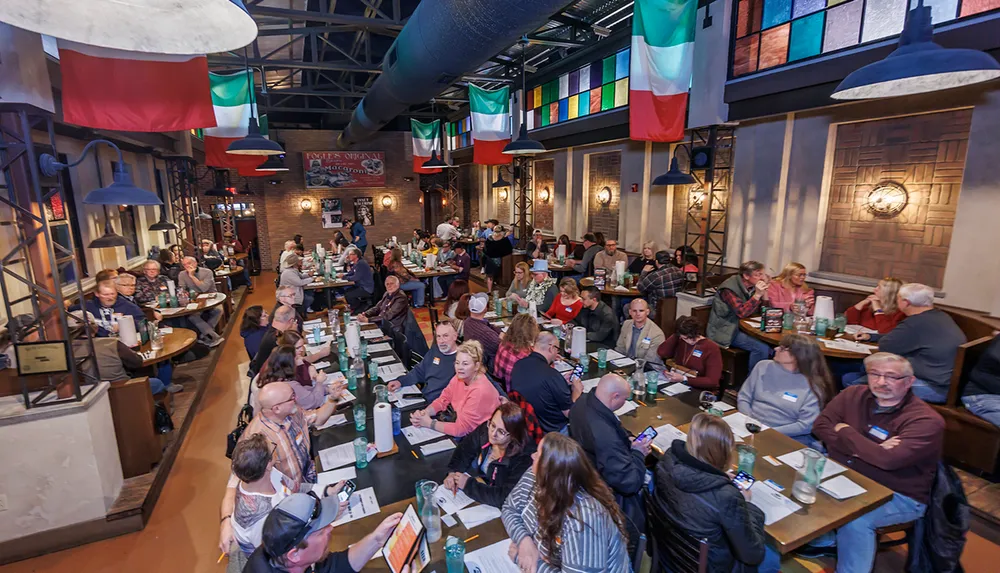 A group of people are gathered in a restaurant setting engaged in conversation and dining with colorful banners hanging from the ceiling