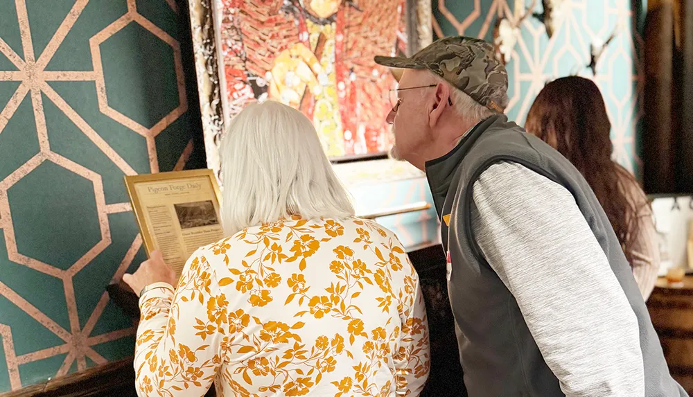 Two people are closely examining a framed document titled Pigeon Forge Daily in a room with patterned walls
