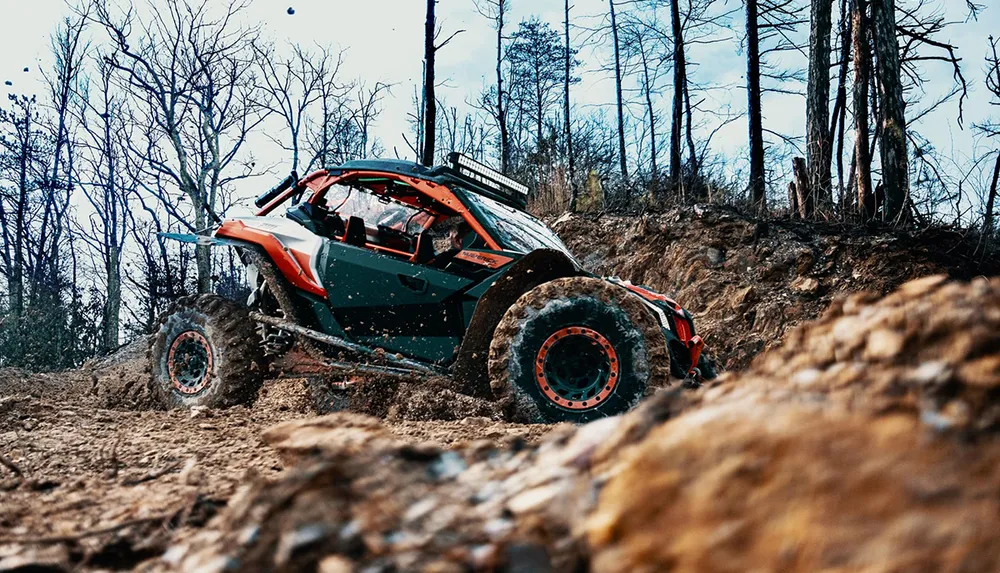An off-road vehicle is navigating a muddy rugged terrain surrounded by bare trees