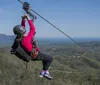 A person wearing a helmet and harness is zip-lining over a vast scenic landscape