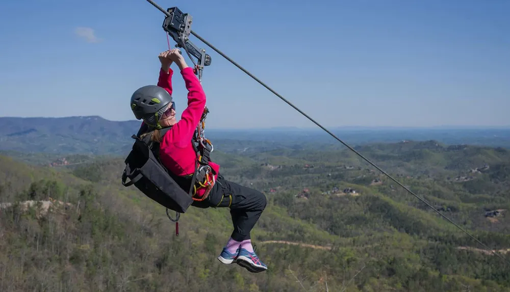 A person wearing a helmet and harness is zip-lining over a vast scenic landscape
