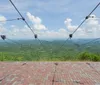 A person wearing a helmet and harness is zip-lining over a vast scenic landscape