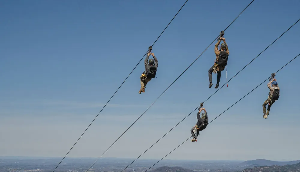 Four people are zip-lining in the sky with a scenic landscape below