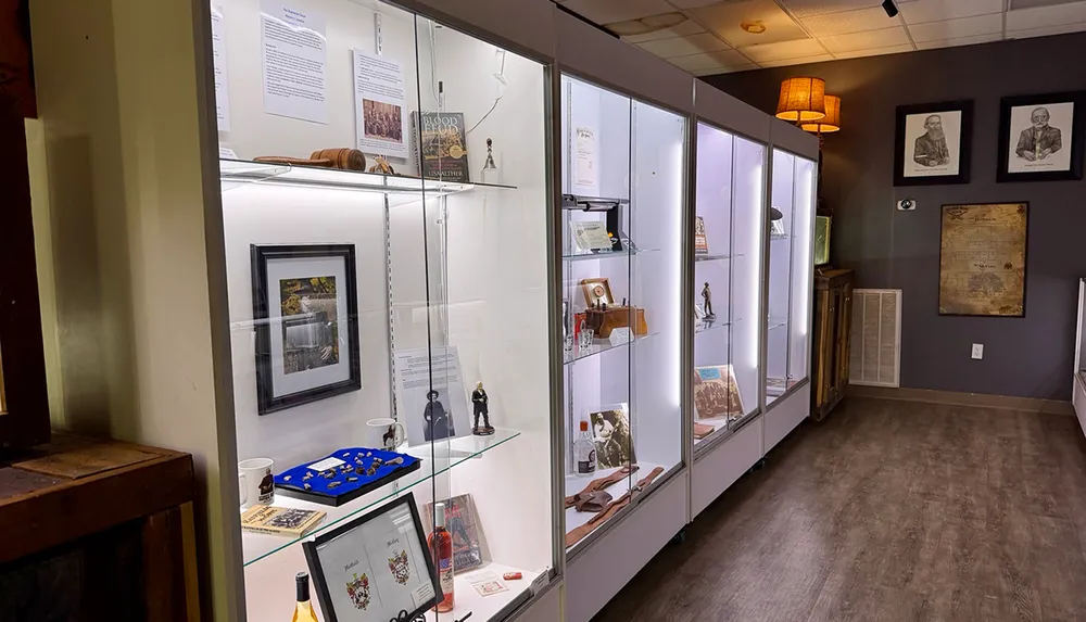 The image shows a well-lit museum display case with various cultural artifacts books and framed pictures situated in an elegantly decorated room with portraits and a map on the wall
