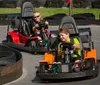 Two children are enjoying themselves while driving go-karts on a track lined with tires