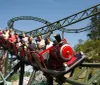 A group of excited people are riding a roller coaster with a red front car that resembles a classic steam engine